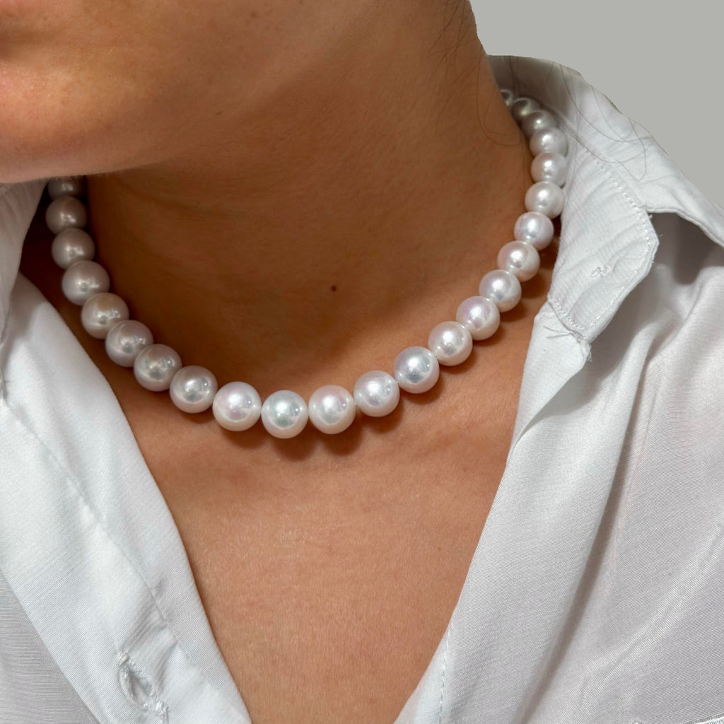 A close-up of a person wearing a classic white freshwater pearl necklace with lustrous, round pearls, styled with a white collared shirt.