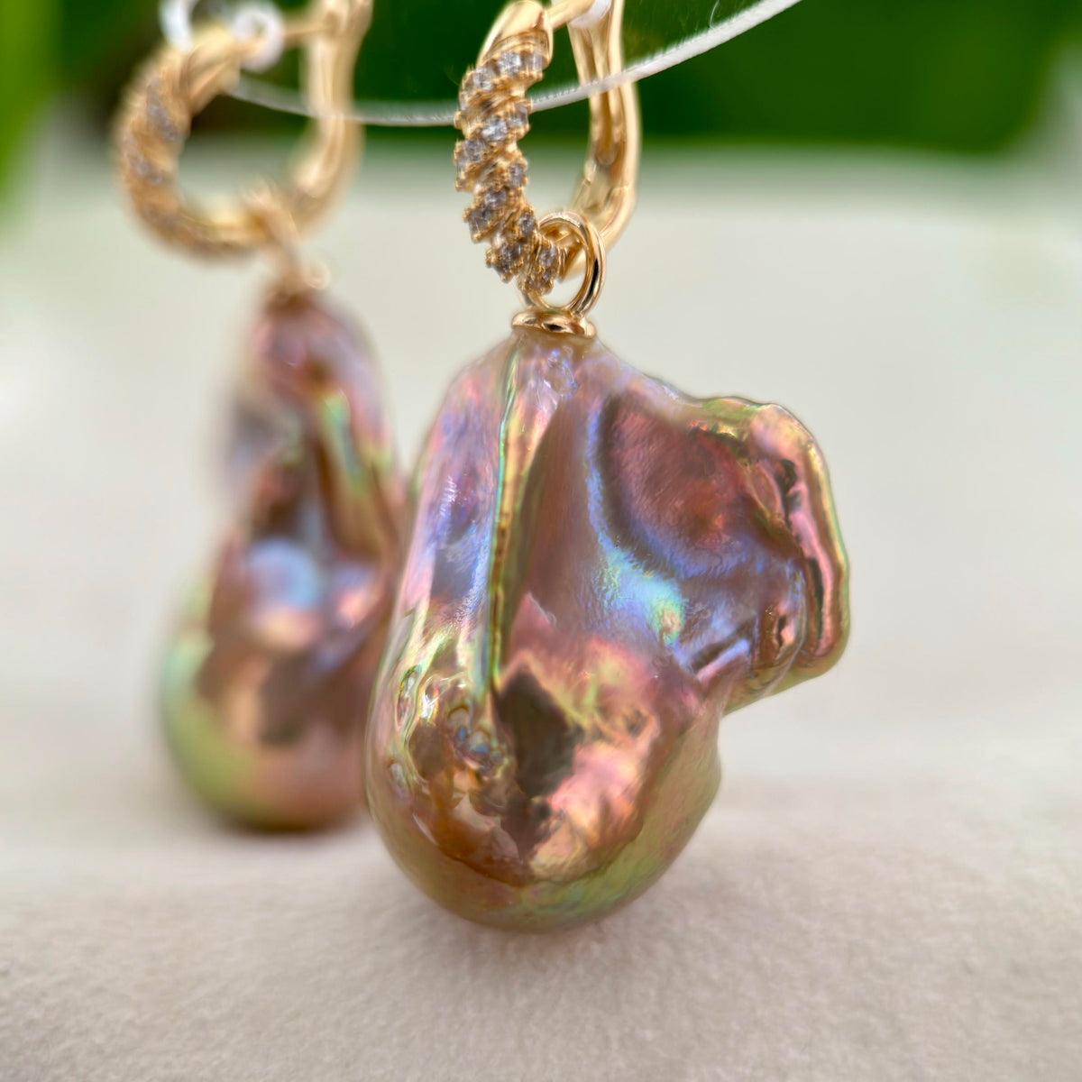 Gold hoop earrings with baroque pearl pendants featuring an iridescent, pearlescent finish with pink, green, and gold tones.