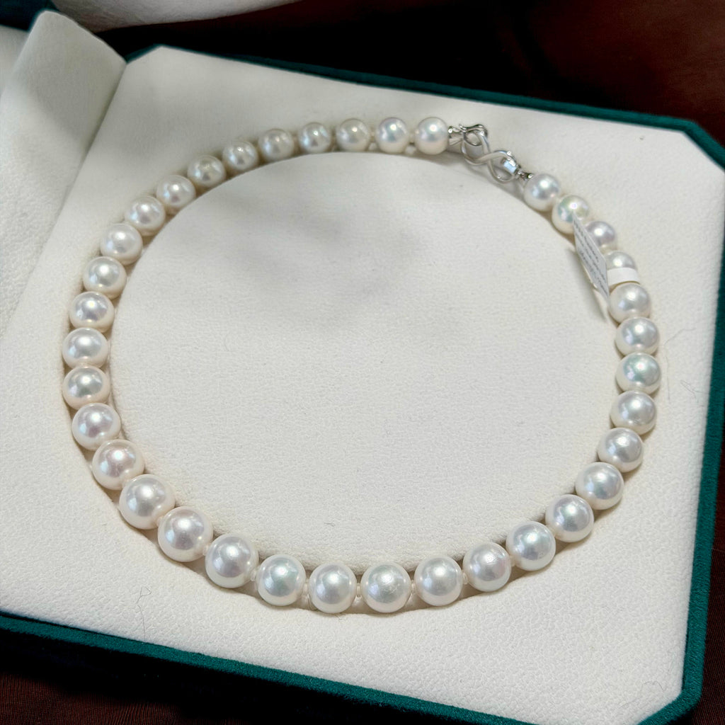 A single-strand pearl necklace with a silver clasp, displayed inside an open white jewelry box with a dark green border.