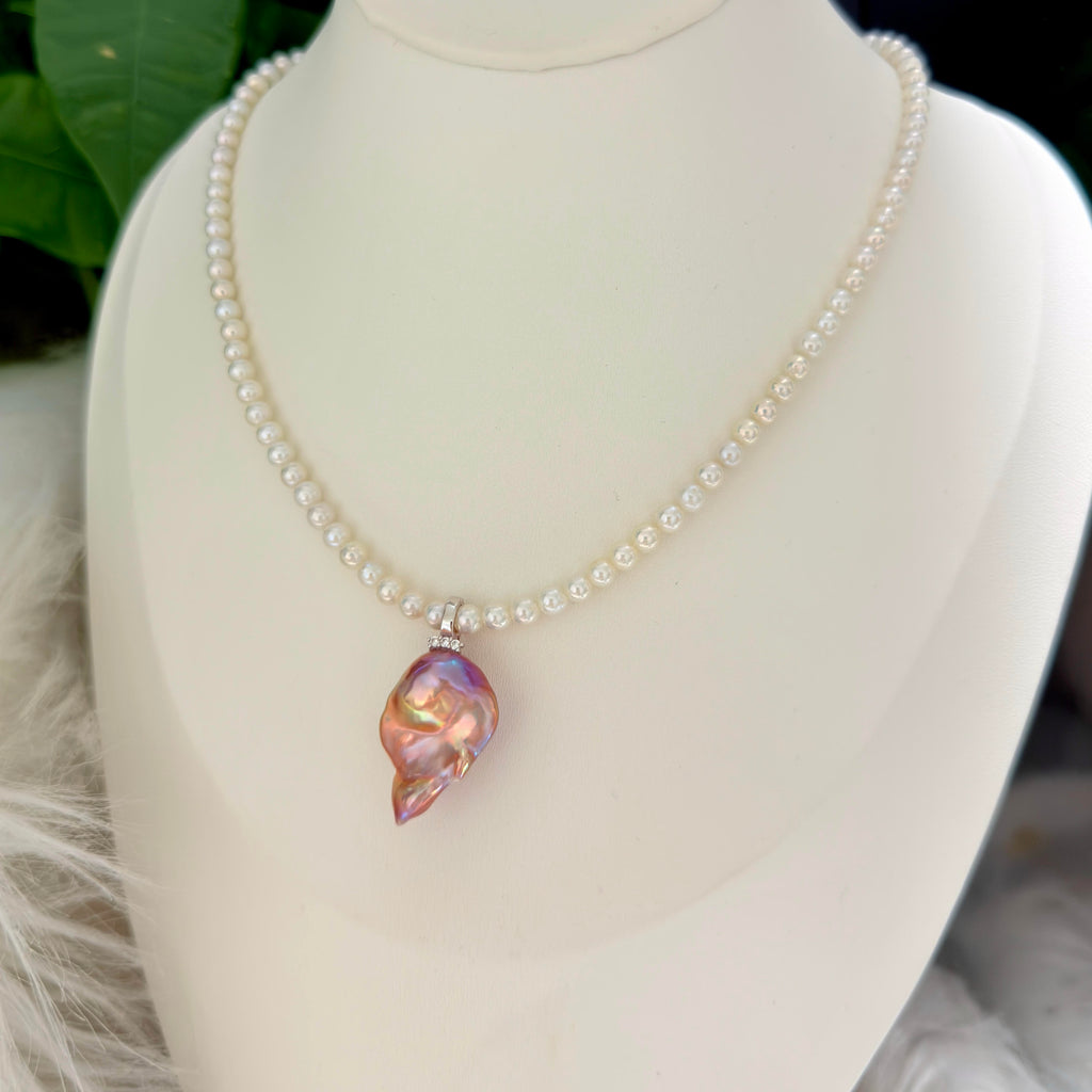 A pearl necklace with a teardrop-shaped iridescent shell pendant, displayed on a cream-colored mannequin bust.