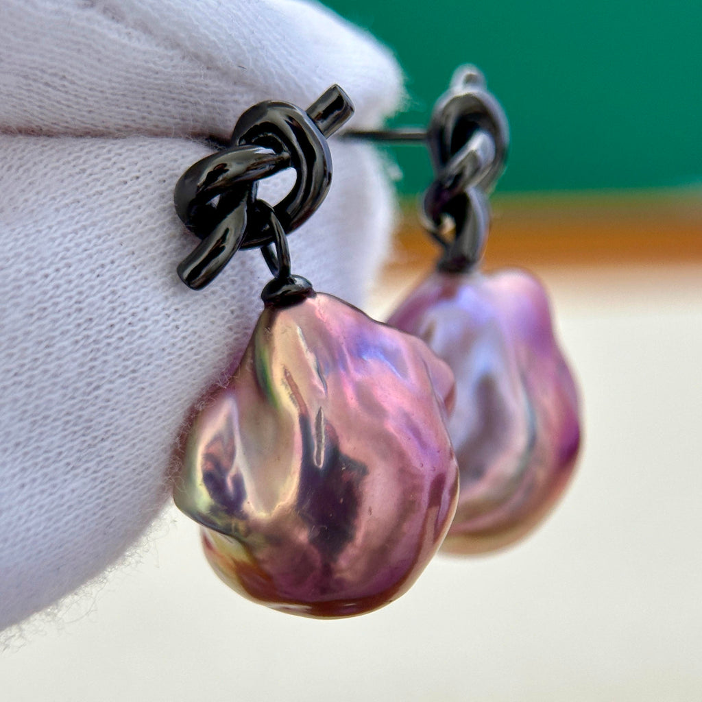 Large freshwater pearl earrings with a black knot-shaped design.
