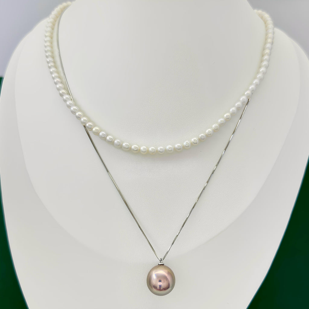 A double-strand pearl necklace displayed on a white jewelry bust. The top strand is a short row of small white pearls, while the bottom strand is a longer silver-tone chain with a single larger iridescent pearl pendant.