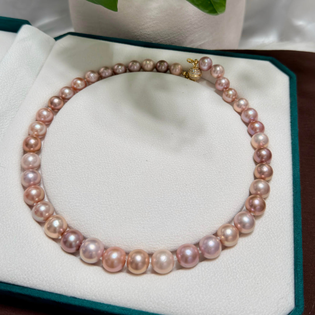 A strand of irregular pink freshwater pearls with a gold clasp, displayed on a white jewelry box cushion.