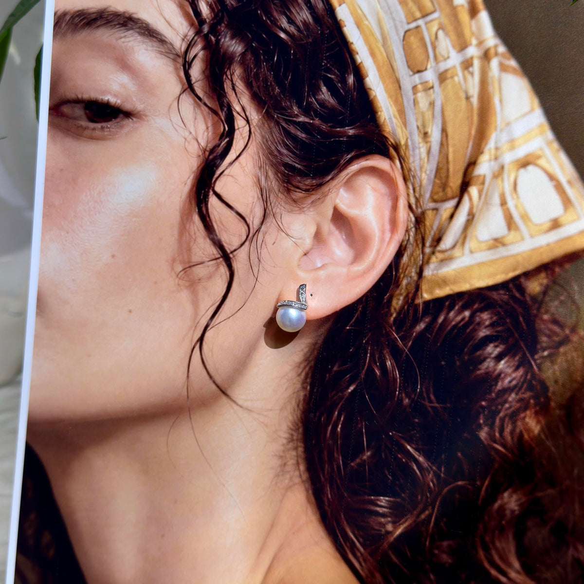 A close-up lifestyle shot of a woman wearing a silver crescent moon earring with a white pearl drop, styled with a patterned gold and white headscarf.