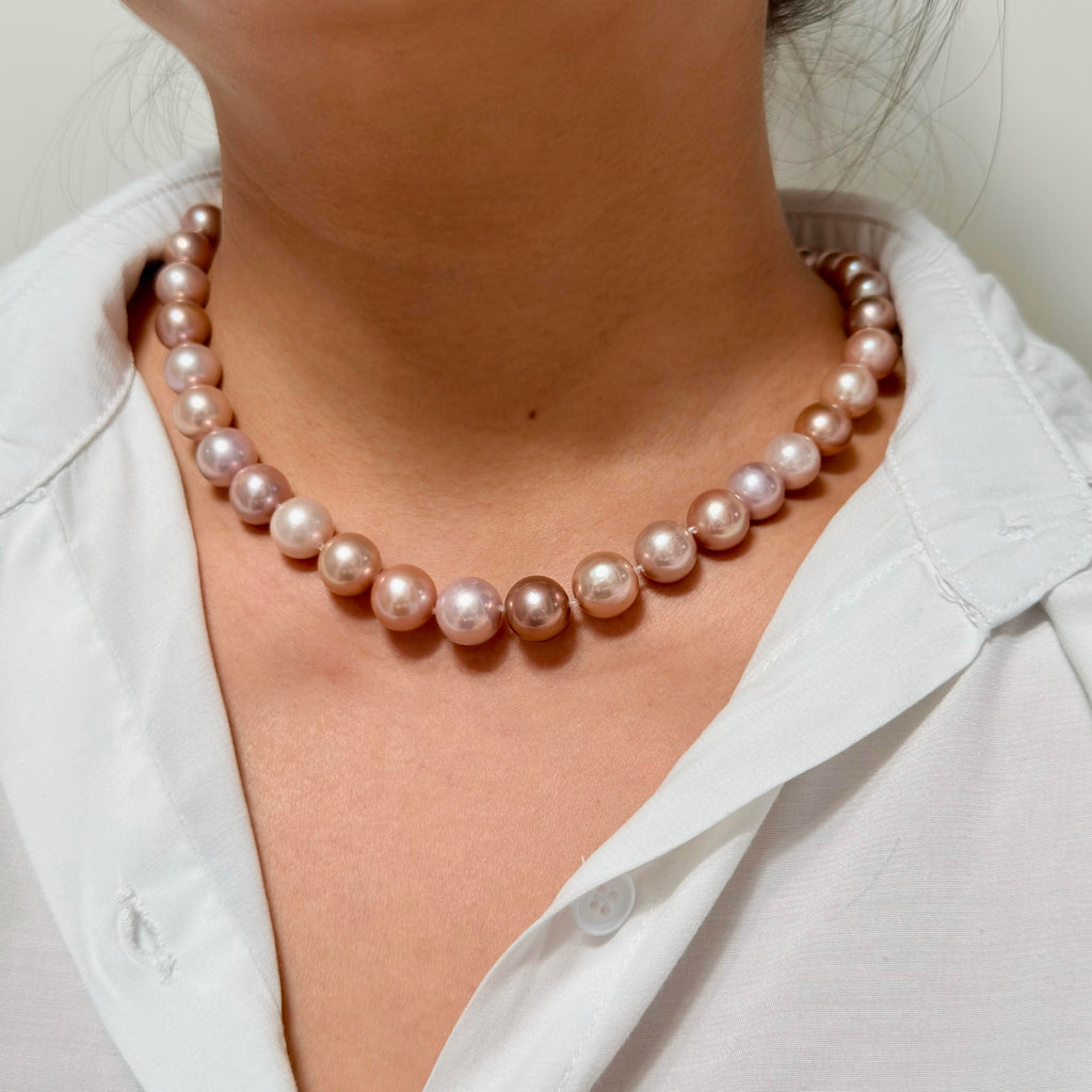 A close-up of a person wearing a strand of round pinkish pearl necklace over a white collared shirt.