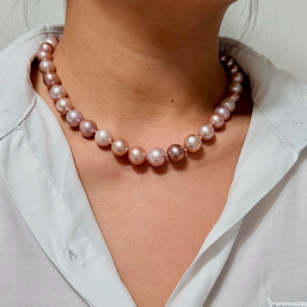 A close-up of a person wearing a single-strand pearl necklace with lustrous pinkish-white beads, paired with a white collared shirt.