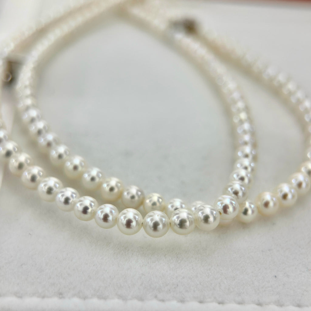 A close-up of a double-strand pearl necklace with white, lustrous round pearl, resting on a light cream-colored textured surface.