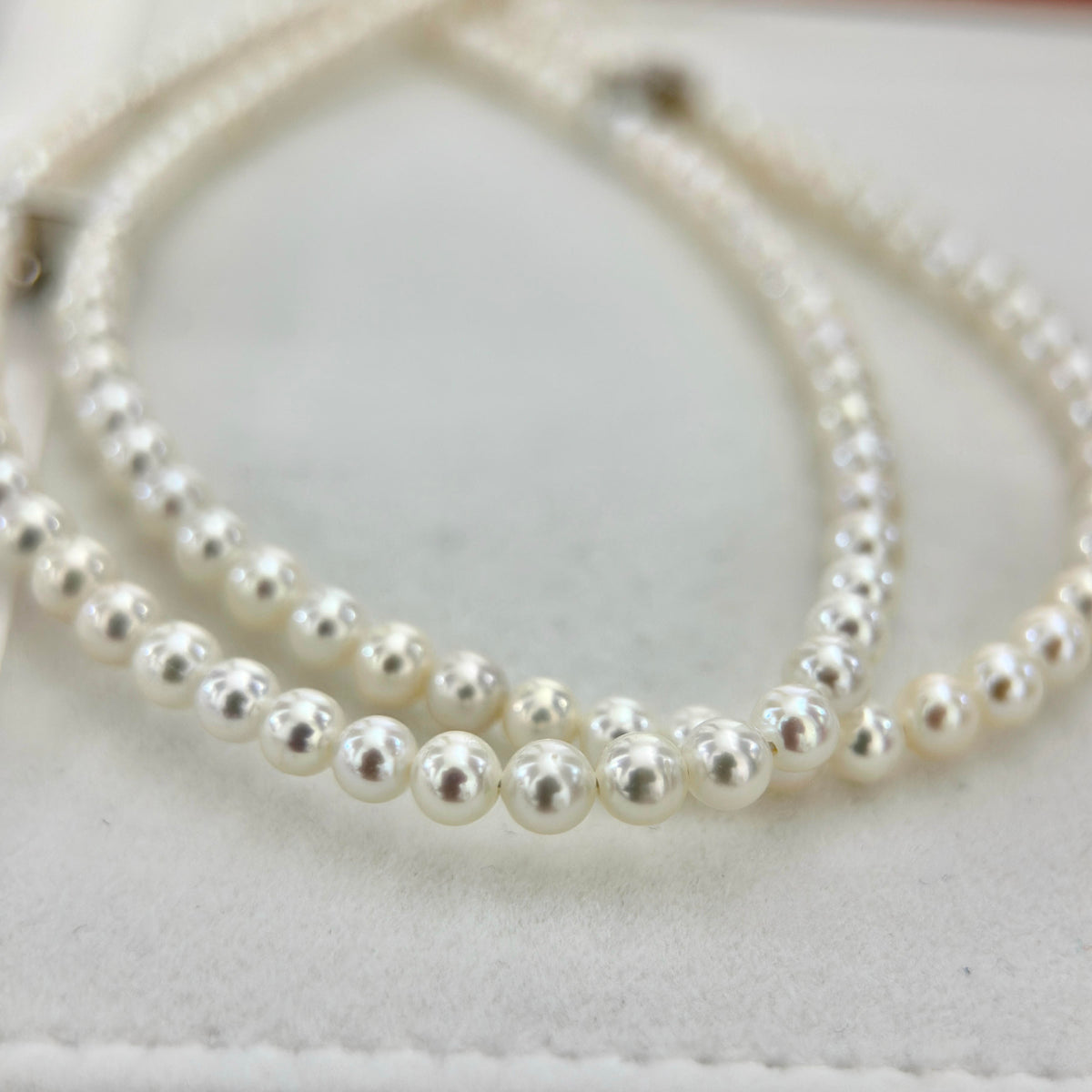 A close-up of a double-strand pearl necklace with white, lustrous round pearl, resting on a light cream-colored textured surface.