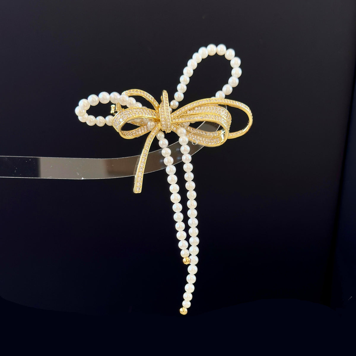 A pearl and gold bow-shaped hair accessory with dangling pearl strands, displayed on a black background.