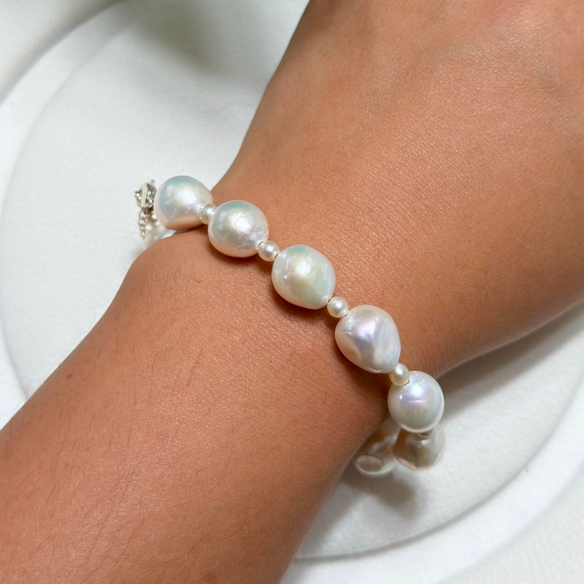 Detailed product view of white ruffled baroque freshwater pearl bracelet with blue-pink iridescence and small pearl accents.