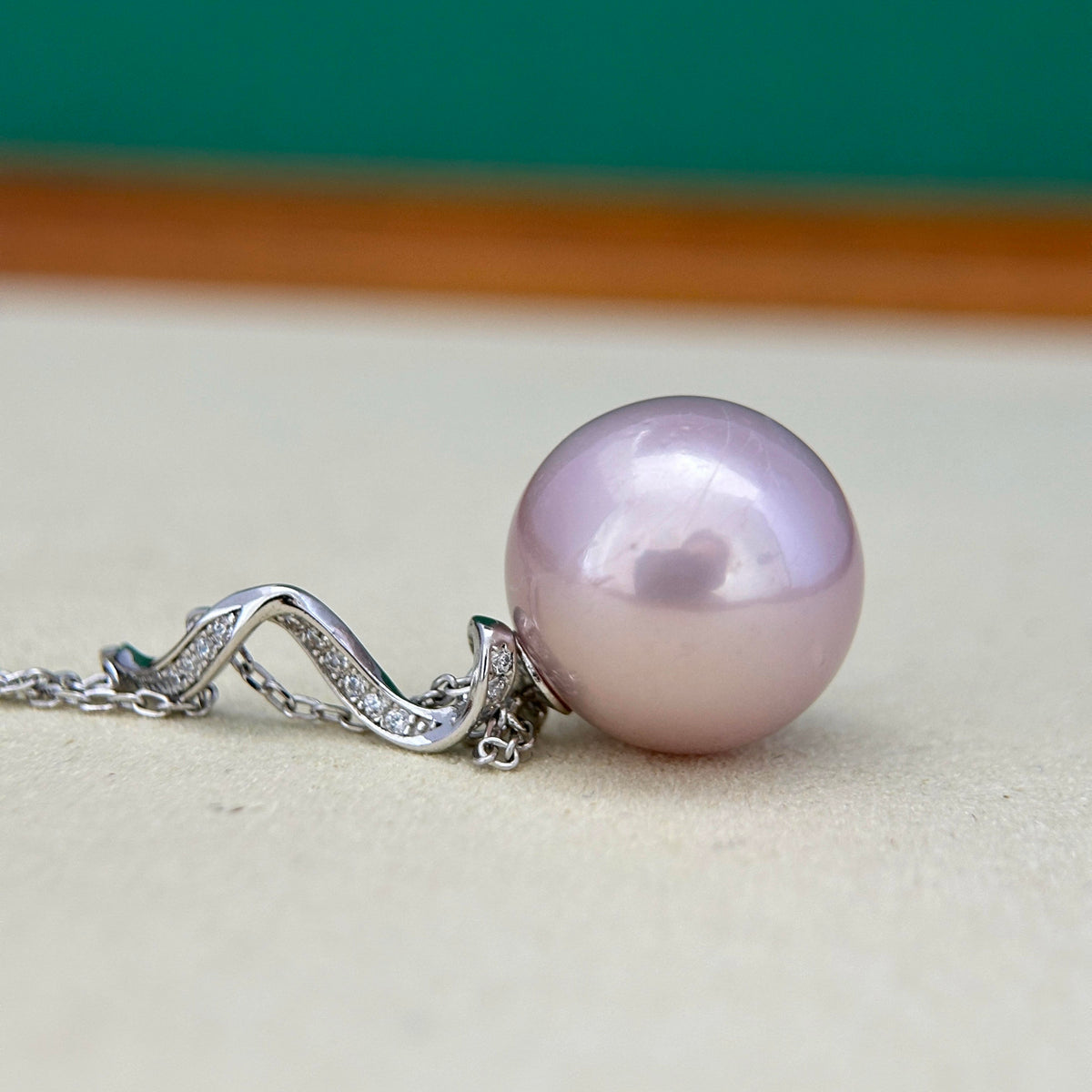 A close-up of a silver necklace featuring a large, smooth, lavender-purple pearl pendant on a delicate chain with small clear stones.