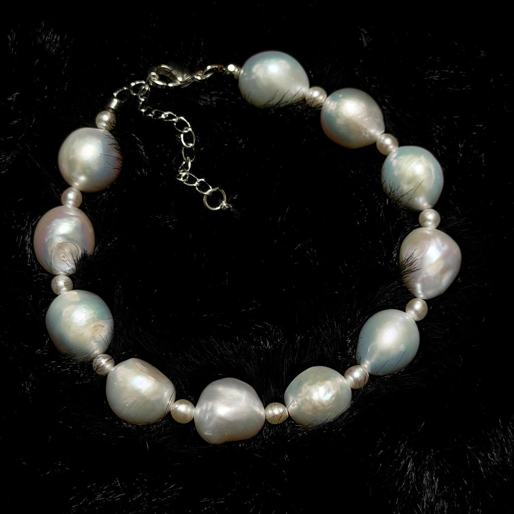 Close-up of white ruffled baroque freshwater pearl bracelet with blue-pink iridescence and small pearl accents.