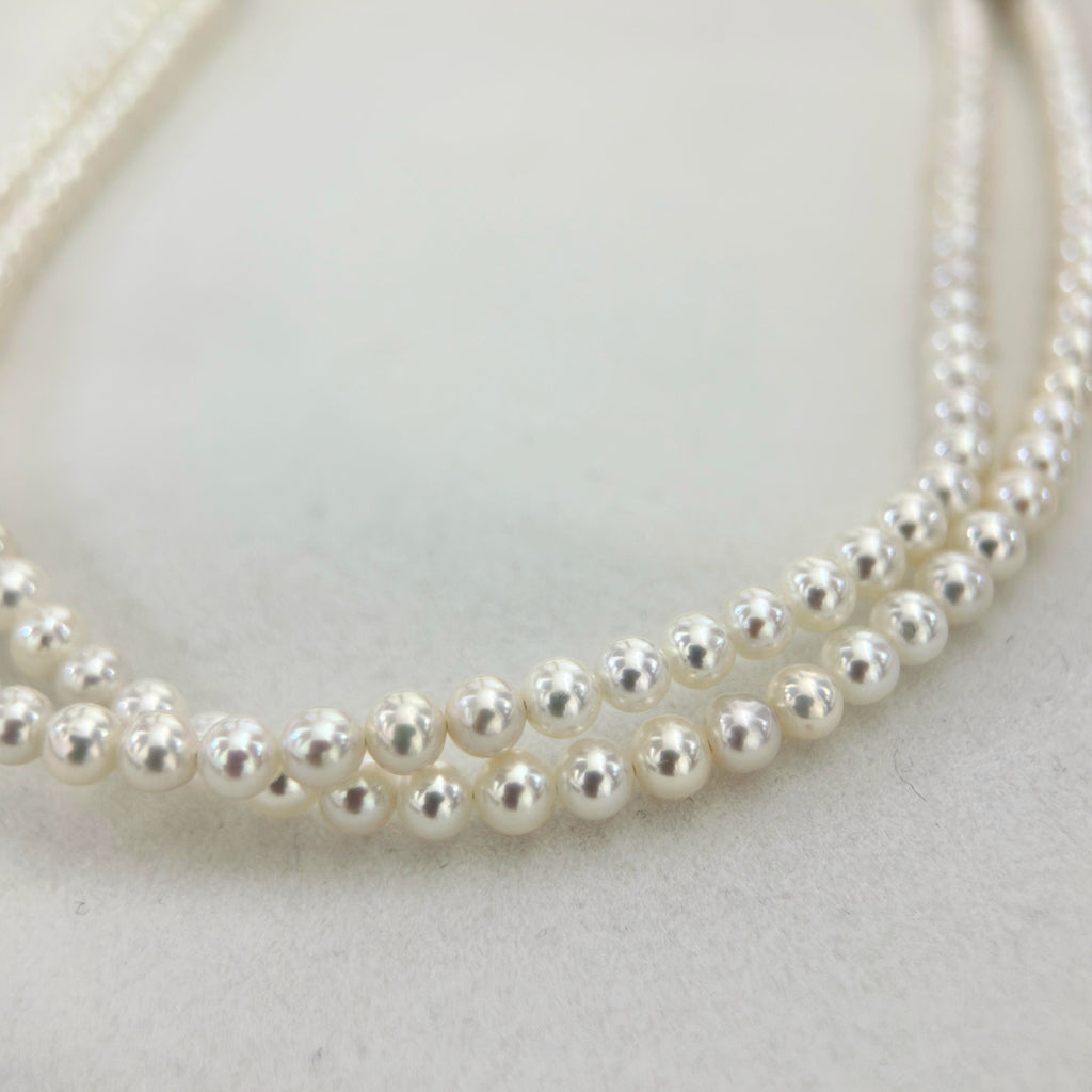 A close-up of a double-strand pearl necklace on a light gray textured background.