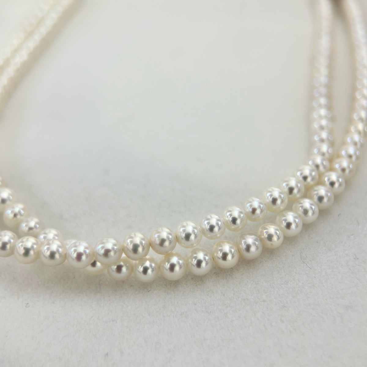 A close-up of a double-strand pearl necklace on a light gray textured background.