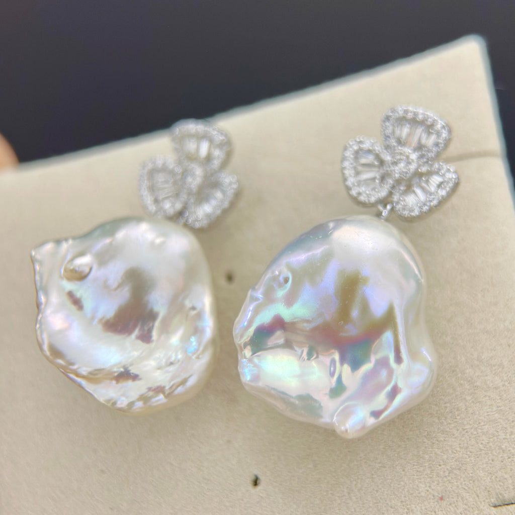 White baroque pearl earrings displaying ethereal blue and pink halos.
