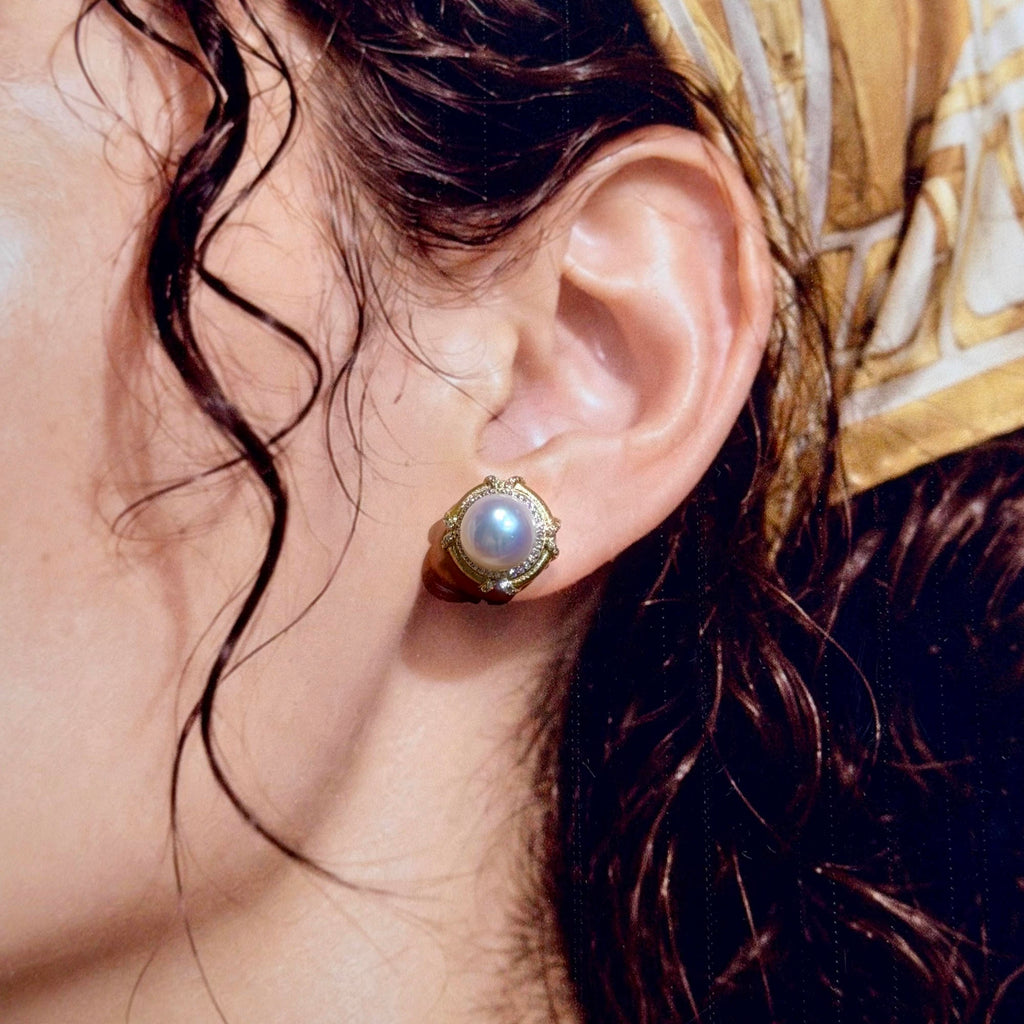 A close-up lifestyle shot of a model wearing a gold-toned stud earring with a white pearl-like center.