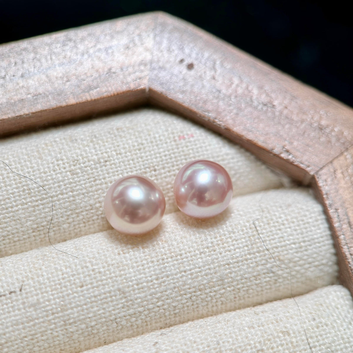 Two round pale pink freshwater pearls displayed on a cream fabric-lined jewelry box.