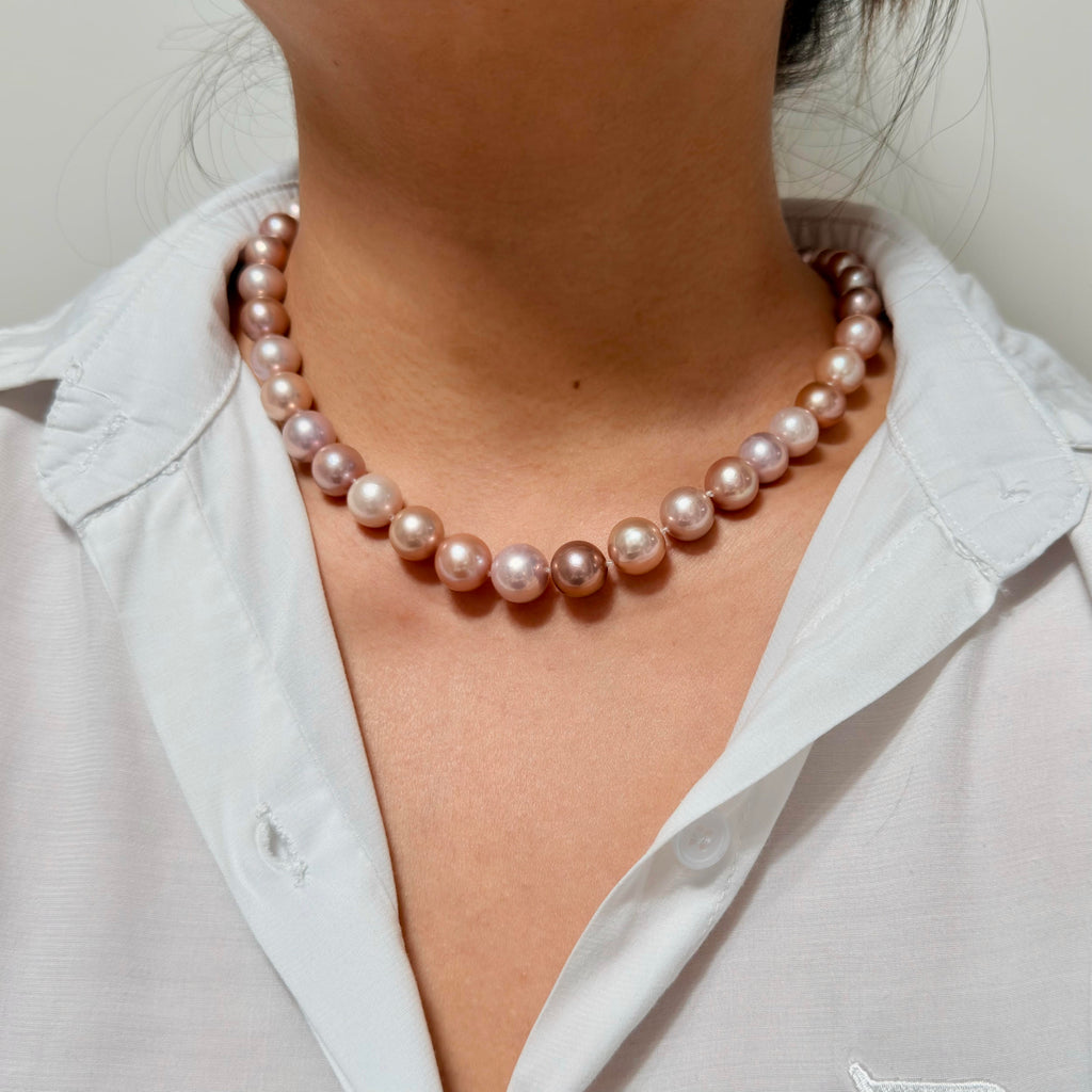 A close-up of a person wearing a strand of lustrous pink freshwater pearls as a necklace, styled with a white collared shirt.