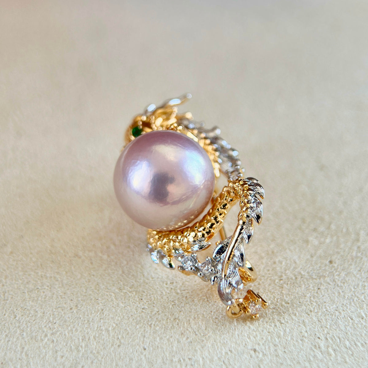 A gold and white gold ring featuring a large lustrous pink pearl and clear crystals, displayed on a textured beige surface.