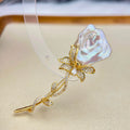 A gold-tone rose-shaped hair claw clip featuring a large, iridescent pearl-like rosebud and a stem paved with small clear stones, displayed on a beige surface.