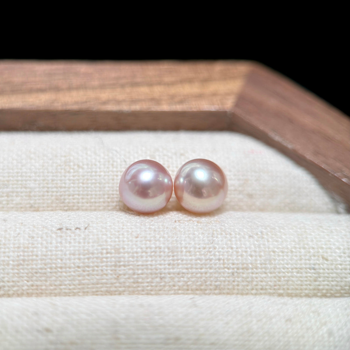 Two round freshwater pearls in a soft pinkish-white luster, displayed on a cream fabric jewelry roll inside a wooden box.