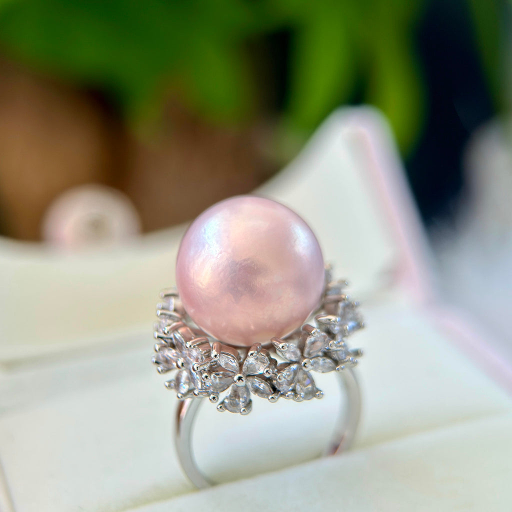 A pink freshwater pearl ring with a silver-toned floral halo setting, displayed on a white jewelry box.