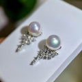 A pair of silver-toned statement earrings featuring a round iridescent pearl at the top of a sparkling crystal cluster, displayed on a white jewelry card.