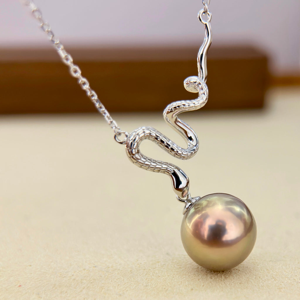 A silver snake pendant necklace draped over a large, lustrous pearl, shown against a soft beige background.