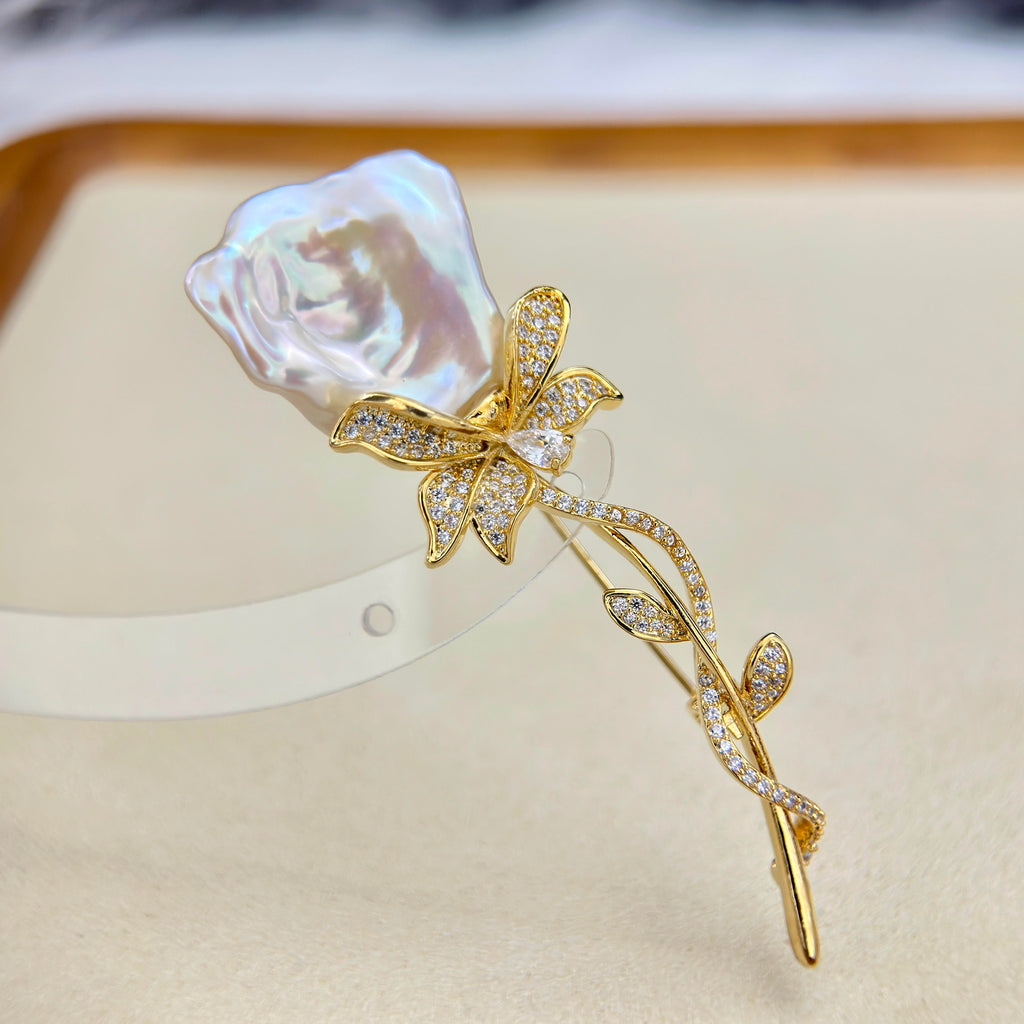 A gold flower-shaped hair claw clip decorated with pavé-set clear crystals and a large, lustrous white pearl rose at the top, displayed on a beige jewelry stand.