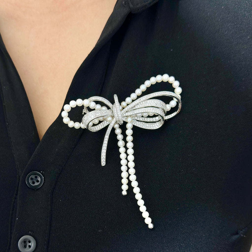 A silver and pearl bow-shaped brooch pin worn on a person's black button-down shirt.
