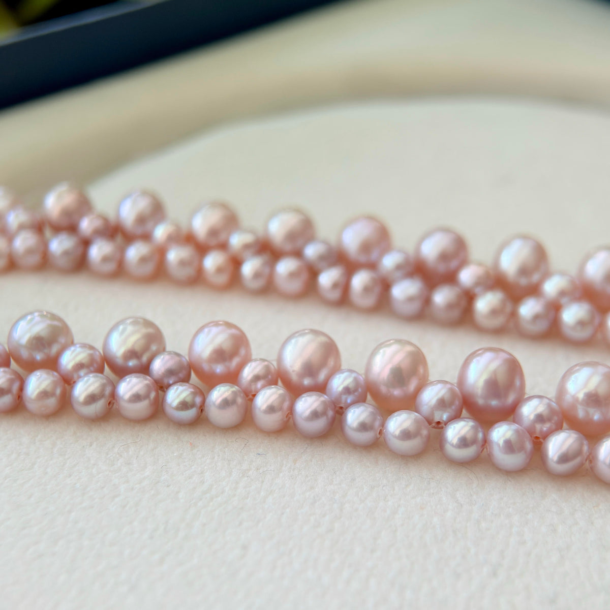 Close-up of strands of pale pink freshwater pearls arranged on a light cream surface.