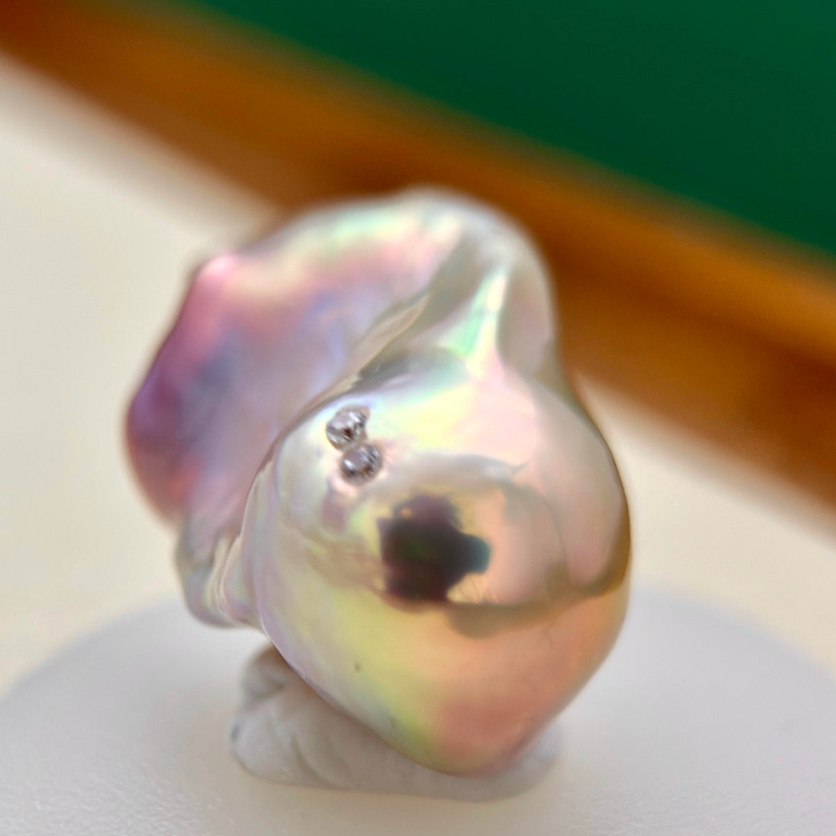 A close-up of an irregular baroque pearl with iridescent pink, purple, and green tones, resting on a white display stand.