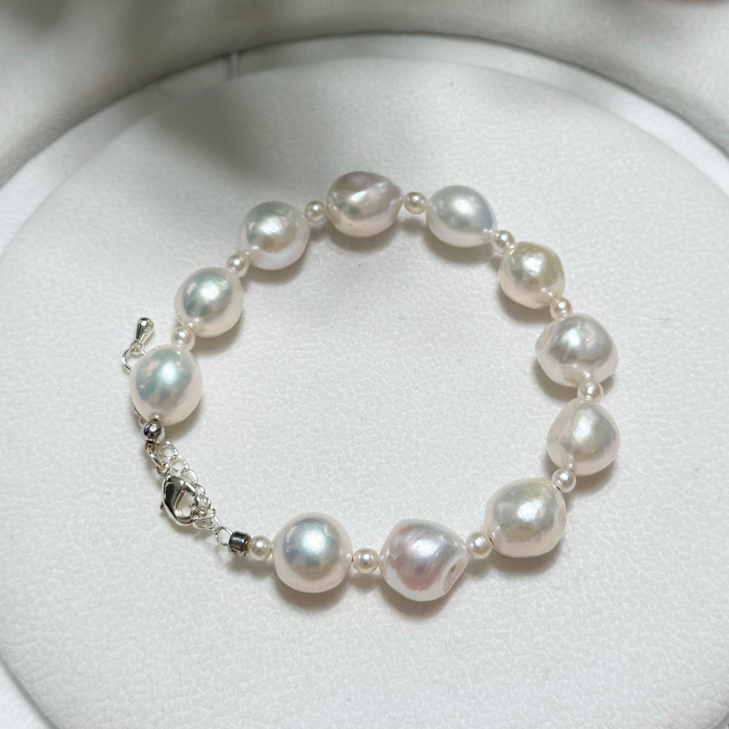 A freshwater baroque pearl bracelet with small silver spacer beads and a silver clasp, displayed on a white circular jewelry stand.