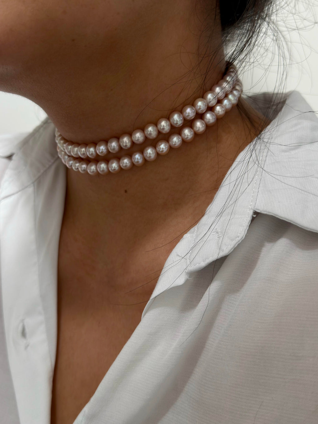 A close-up of a model wearing a double-strand pearl choker necklace with a white collared shirt.
