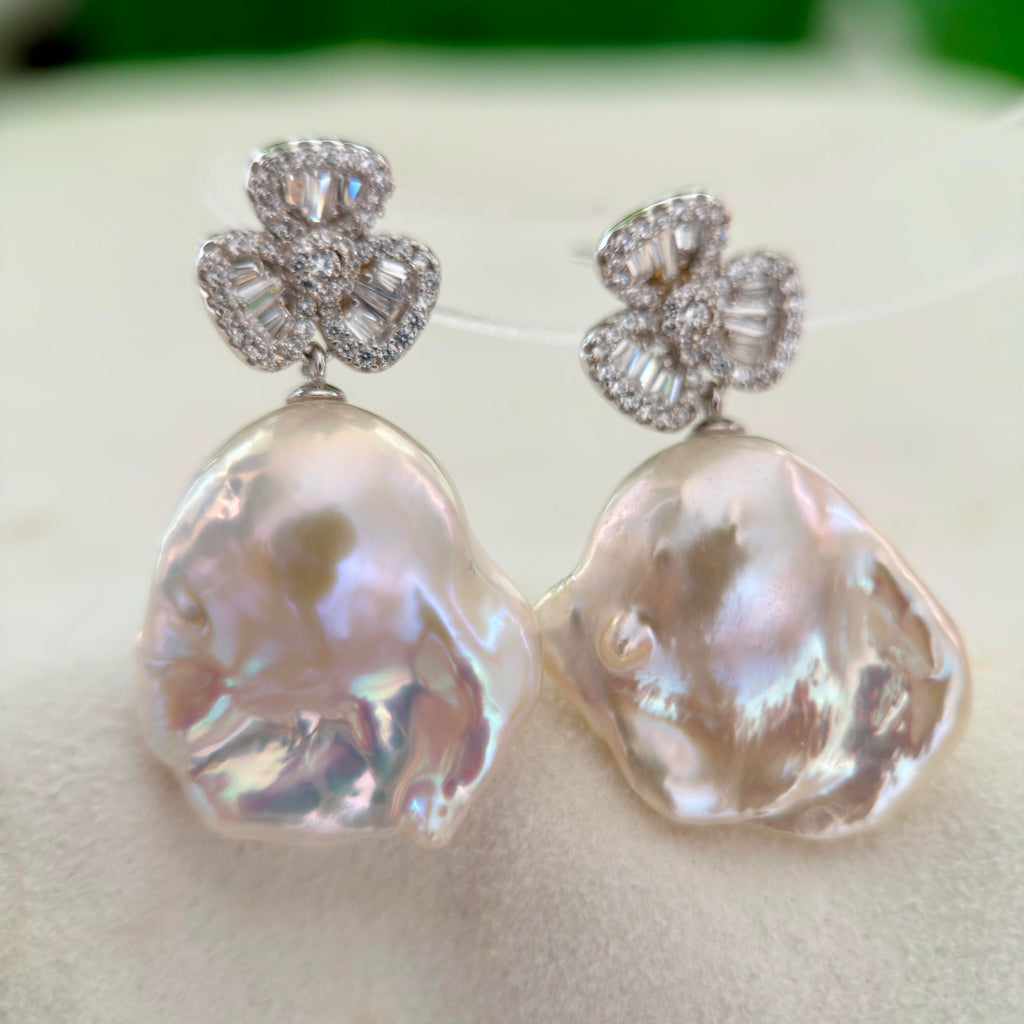Large white baroque pearl earrings with luminous iridescent halos.
