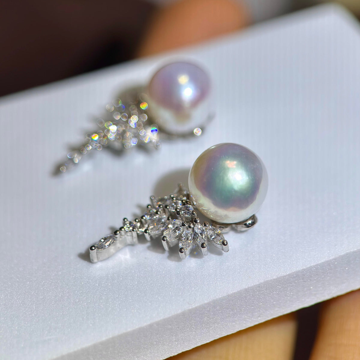 A pair of silver-toned statement earrings featuring large iridescent freshwater pearls and sparkling clear crystal clusters, displayed on a white card.