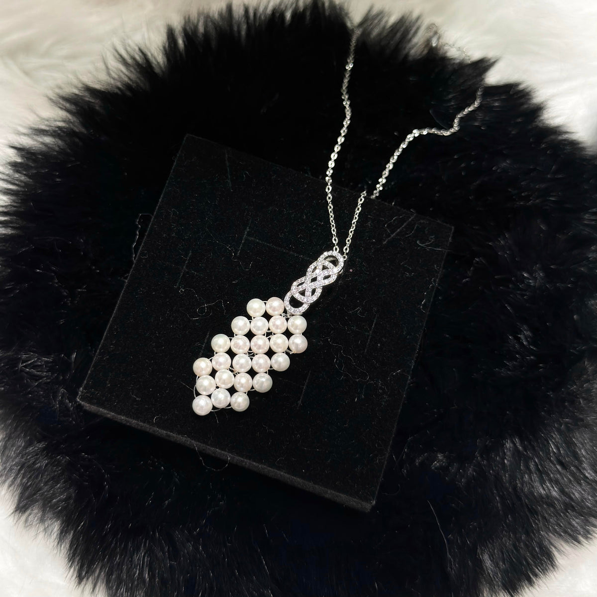 Sterling silver pearl necklace with a sparkling bow detail and elegant woven design.