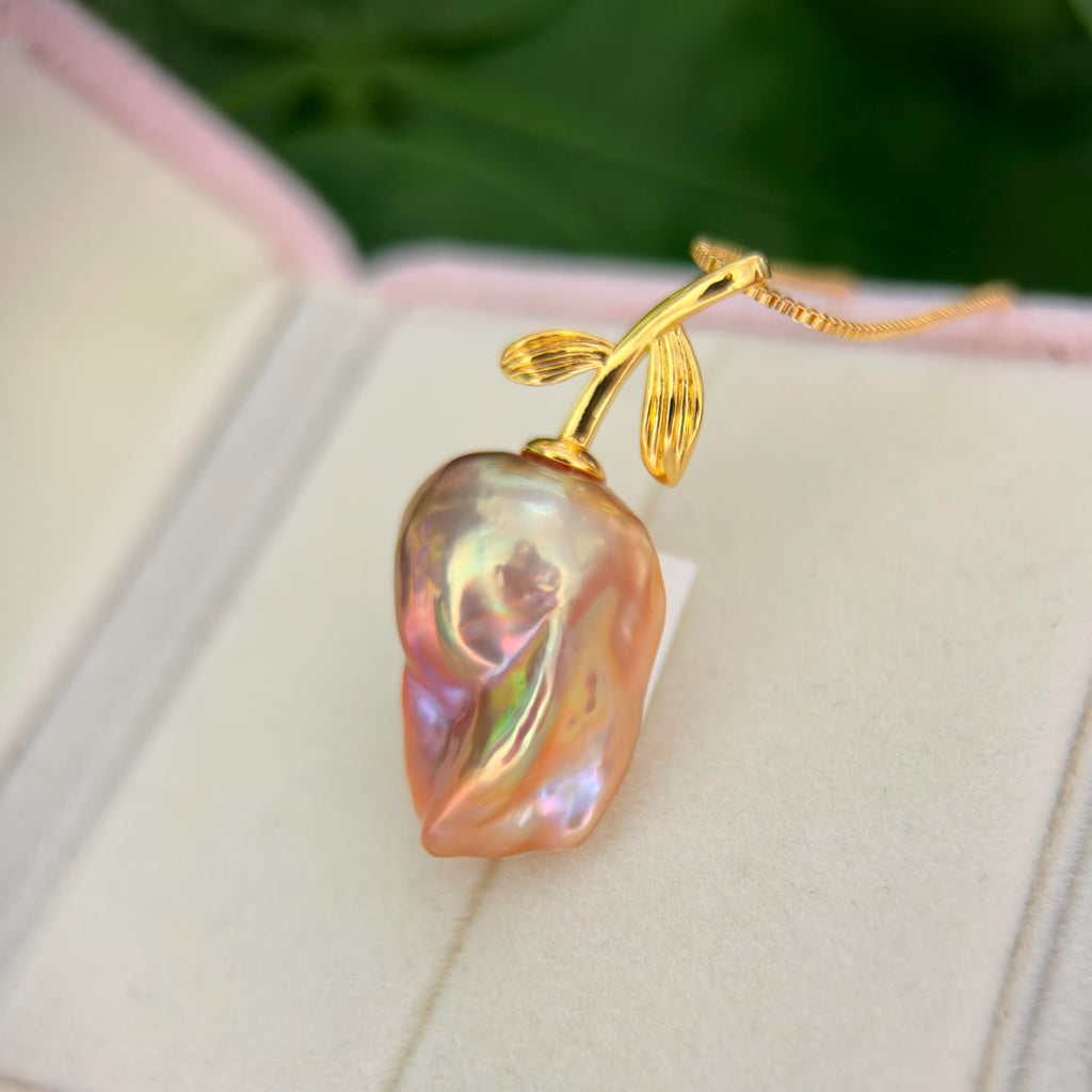 A gold pendant necklace shaped like a pear with a baroque pearl inside, resting on a white jewelry box.