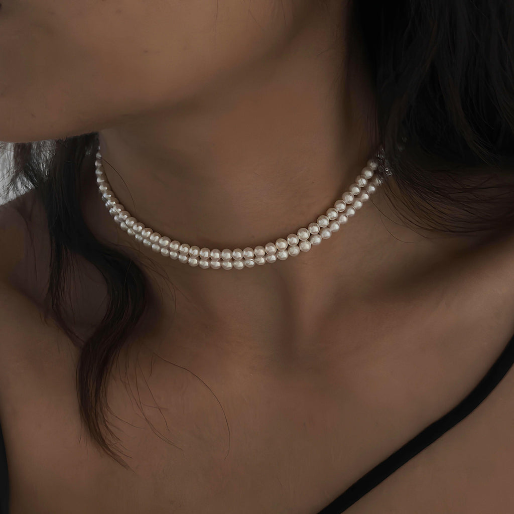 A close-up of a model wearing a double-strand pearl choker necklace, showing the delicate curve of the necklace against the neck.