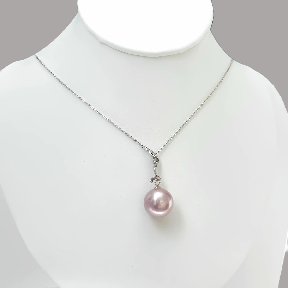 A silver chain necklace with a single lustrous pink pearl pendant, displayed on a white jewelry bust against a light gray background.