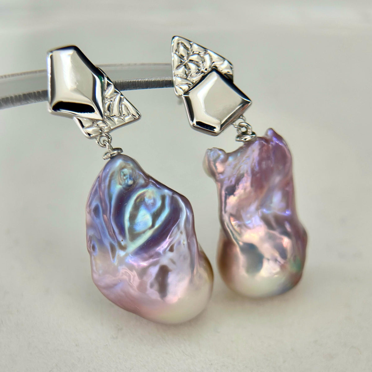 Natural pearl lustre shown on purple-blue baroque freshwater pearl earrings with asymmetric geometric sterling silver frames.