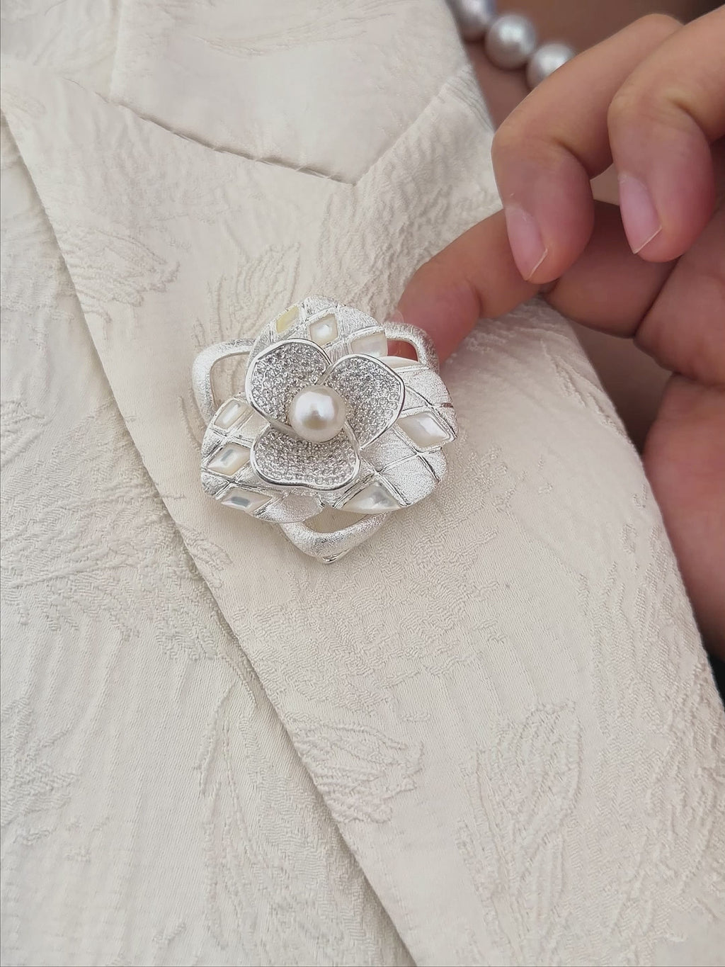 Model wearing an elegant freshwater pearl camellia brooch with a cool white pearl center.