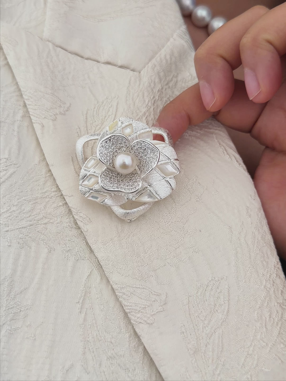 Model wearing an elegant freshwater pearl camellia brooch with a cool white pearl center.
