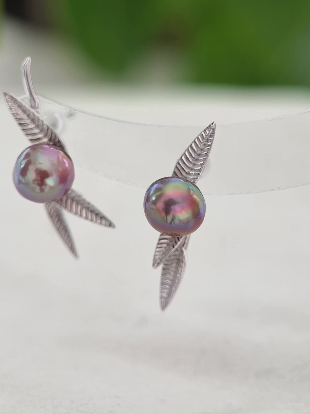Nature-inspired pearl stud earrings with purple iridescent halos.