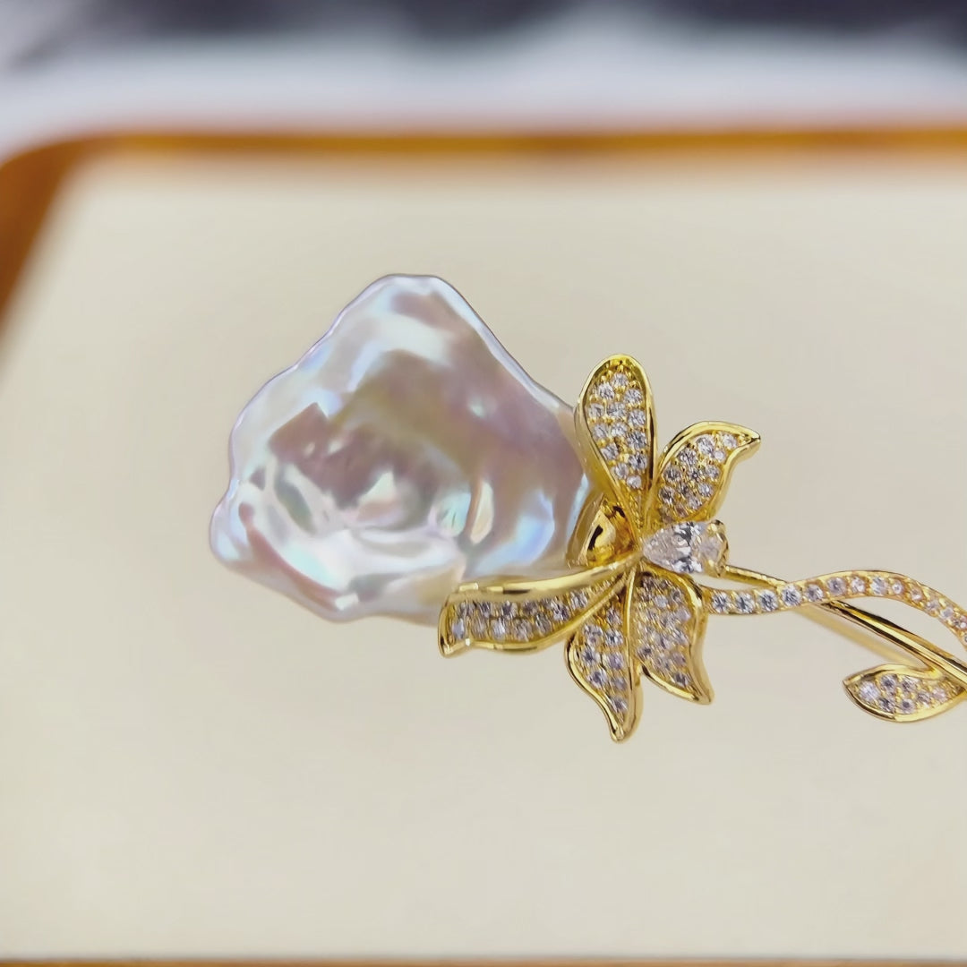 Rose-shaped white baroque freshwater pearl floral brooch with gold-plated setting.
White baroque pearl brooch displaying blue pink green and purple iridescent halos.